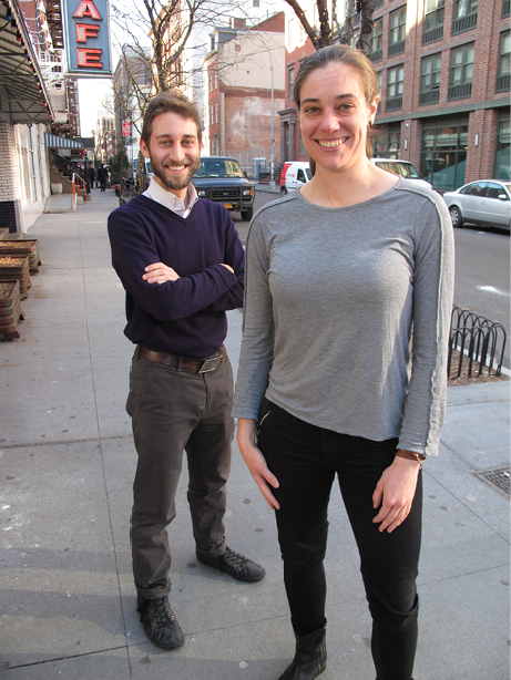 A young woman and man are standing on a city footpath.