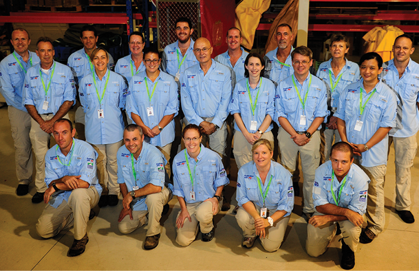 20 men and women wearing blue and beige uniforms and green lanyards.