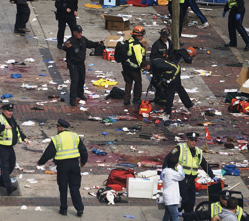 A photo of the street after the Boston bombing. Police, firefighters and other emergency management personnel are directing people and talking to each other. There is a lot rubbish on the street.