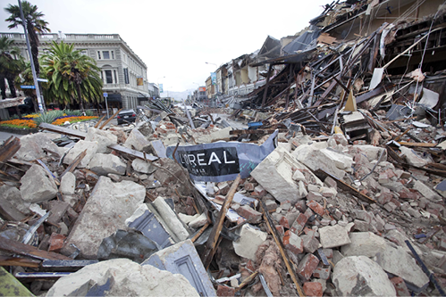 A photo of a street damaged in a New Zealand earthquake. There is a lot of rubble and debris on the ground, and the street sign is tangled in the debris.