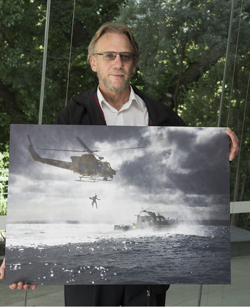 A photo of Jason Harris with his photo ‘By air and by sea’, which was a finalist in the 2016 Resilient Australia National Photography Award. His photo shows a helicopter an boat involved in Volunteer Marine Rescue training exercises.