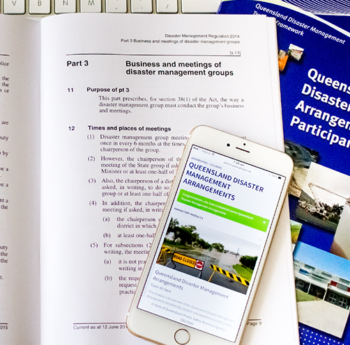A photo of several resources used in Queensland Disaster Management Training, comprising training manuals and a Queensland Disaster Management Arrangements app on a mobile phone.