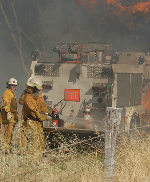 A photo of three CFA firefighters alongside their fire truck, putting out a grass fire.
