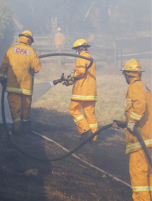 A photo of three CFA firefighters putting out a fire with a fire hose.