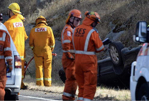 Photo of several people in Country Fire Authority and State Emergency Service uniforms at an incident where a car is lying on its roof next to a country road.
