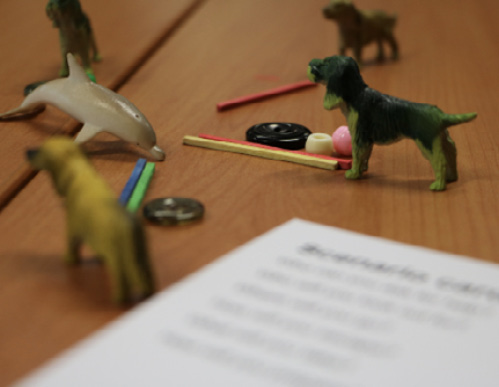 Photo of small items on a table: toy dogs and dolphin, buttons, beads and coloured rods.