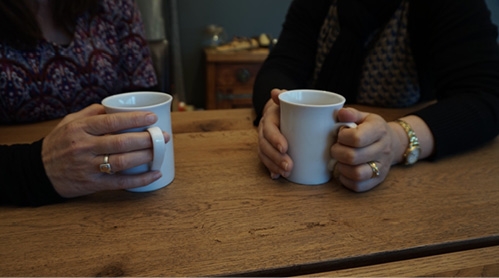 Photo of two sets of hands holding coffee mugs on a table.